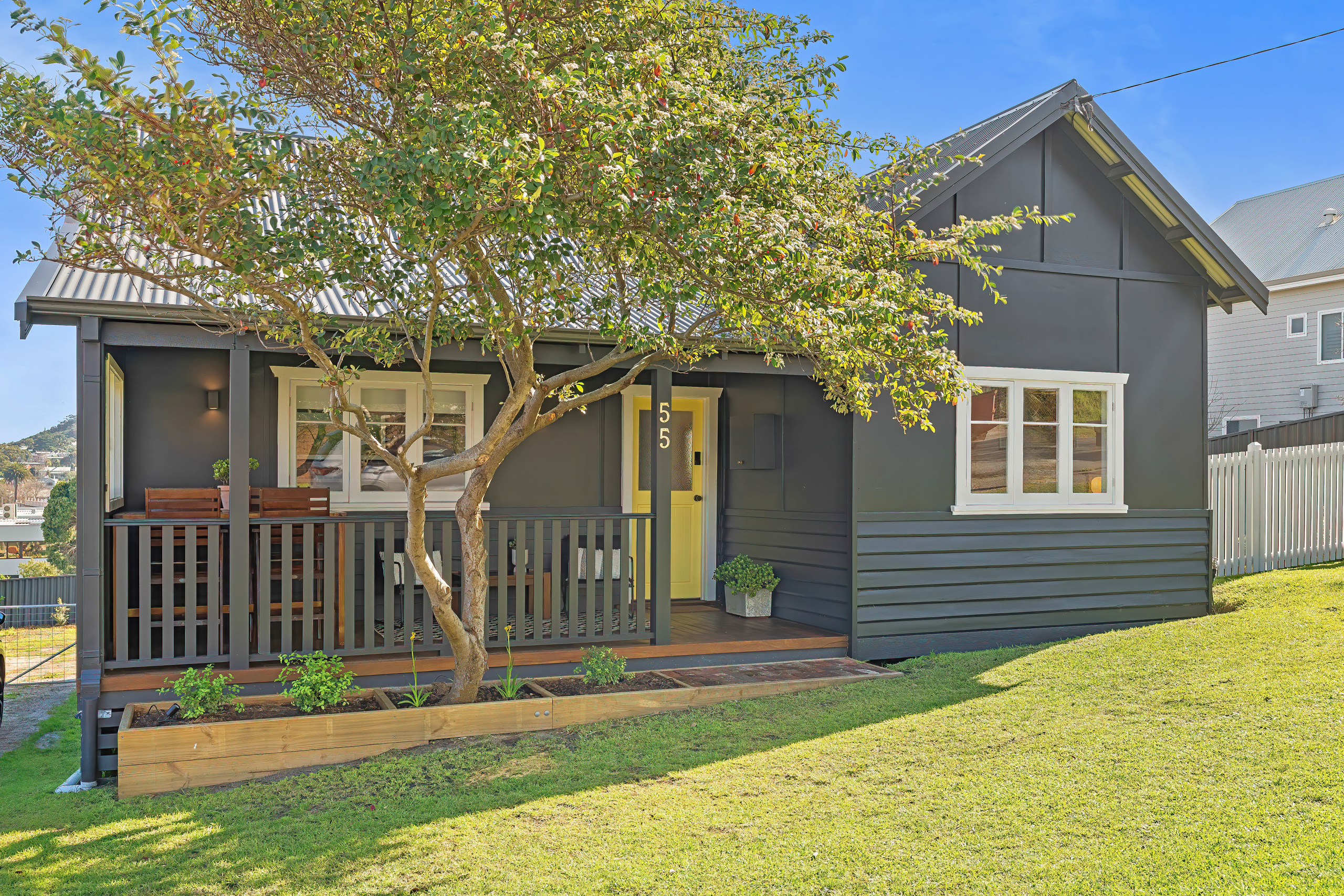 Full front exterior of The Yellow Door on Spencer: dark cottage facade, yellow front door, covered porch and mature garden tree