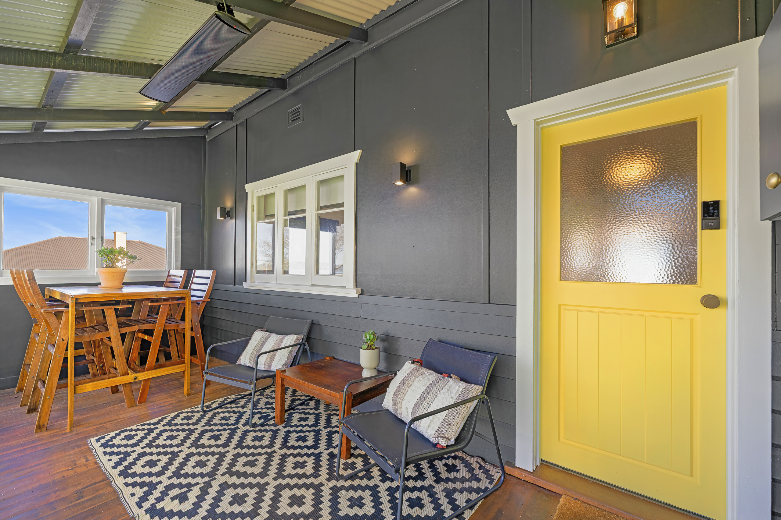 Covered front porch with outdoor dining table, lounge chairs, overhead heater and yellow front door
