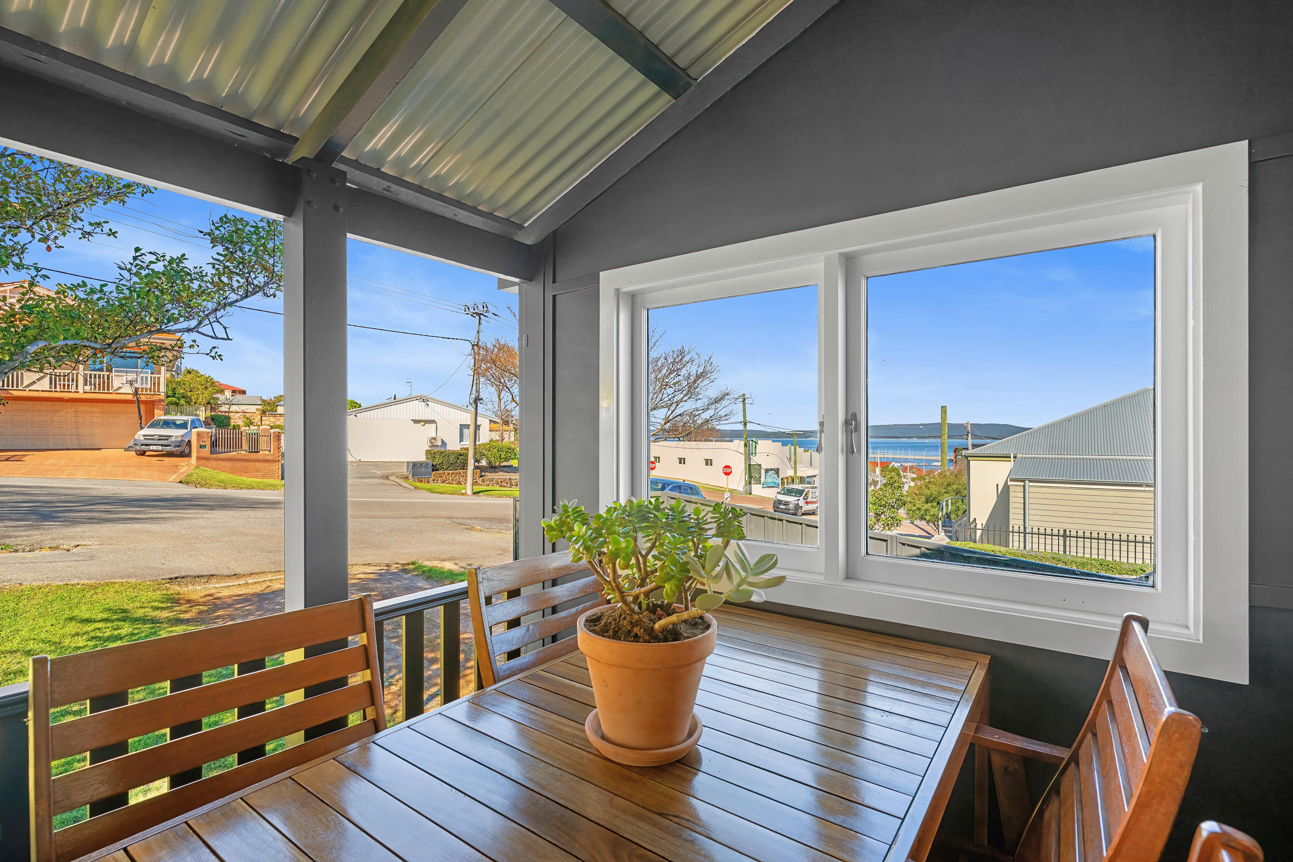 Porch dining table with terracotta pot plant and harbour view through window