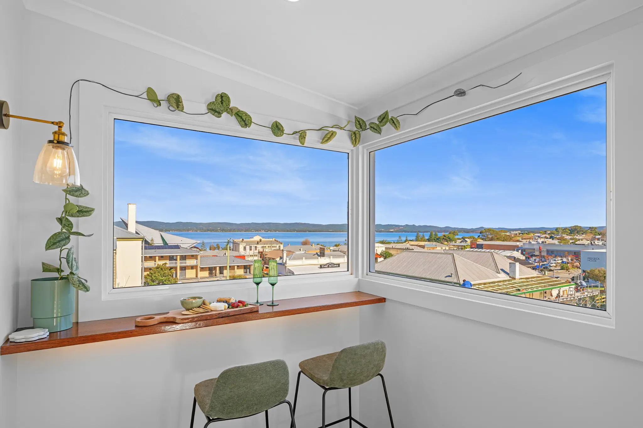 Corner view bar with two stools, cheese board and green wine glasses overlooking Albany harbour on a clear day