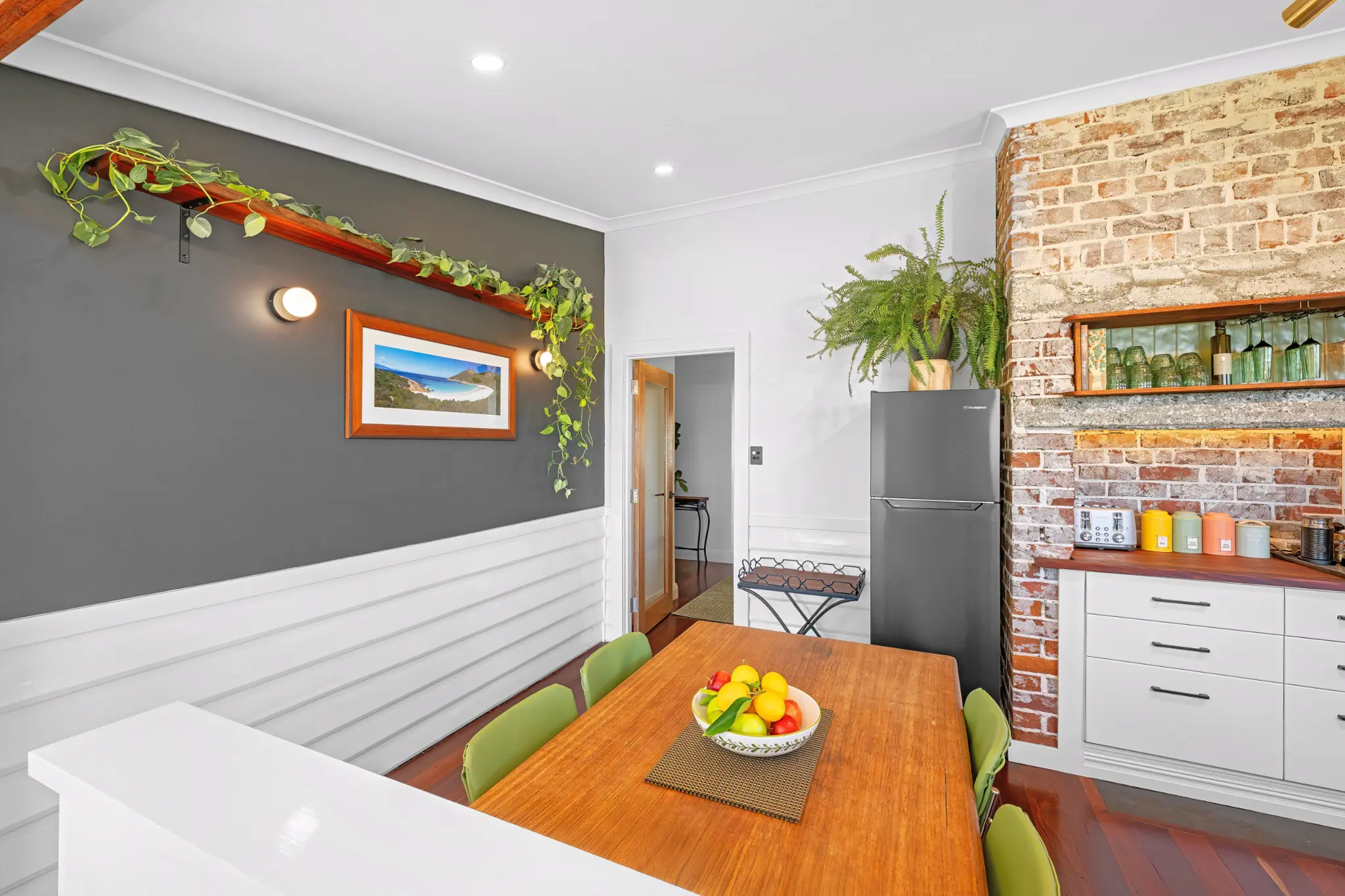 Dining table with green chairs beneath grey feature wall and exposed brick chimney