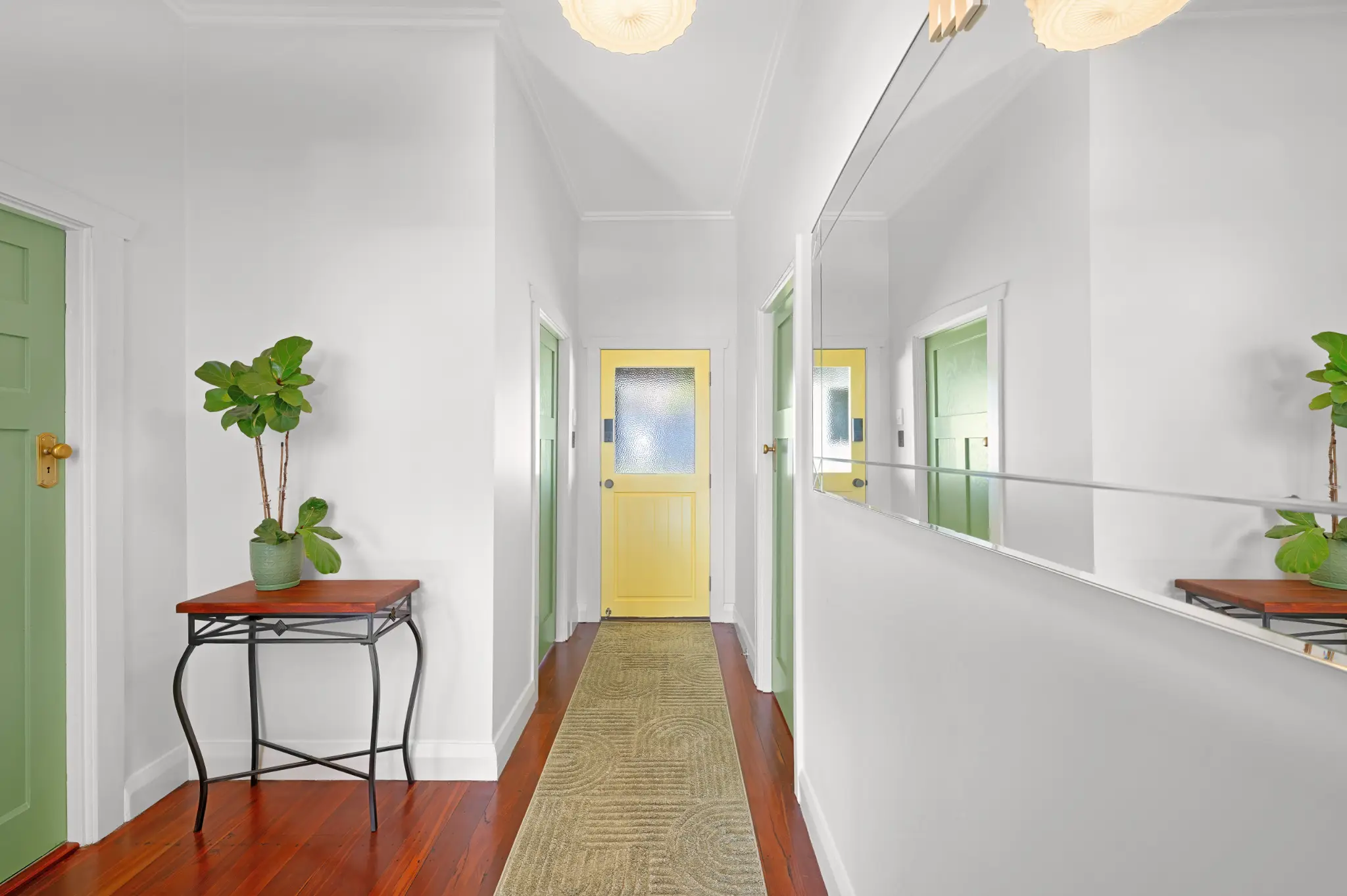 Central hallway with high ceilings, polished jarrah floors, green doors and yellow back door at the end