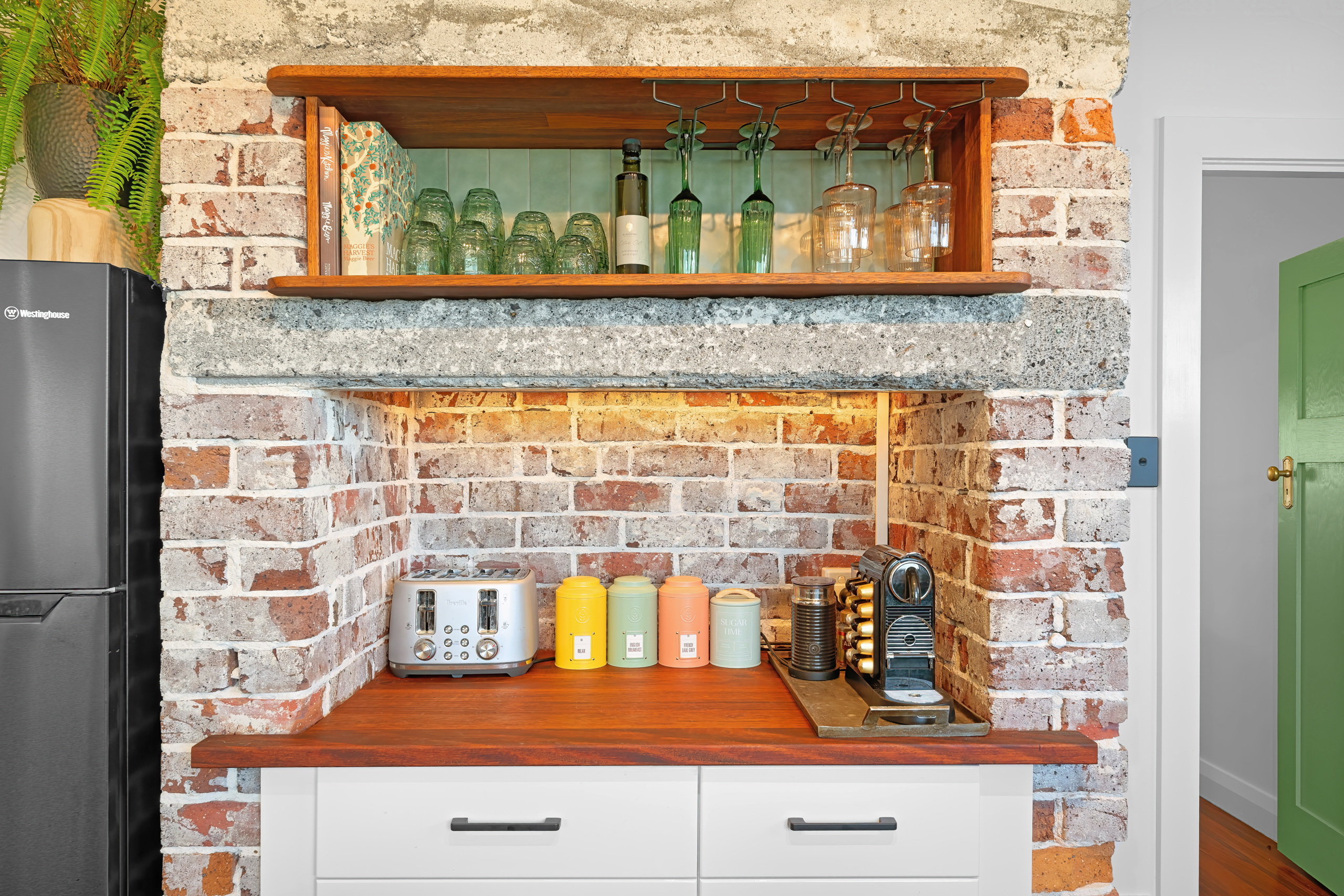 Exposed brick coffee station with Nespresso machine, toaster, colourful canisters and wine glasses