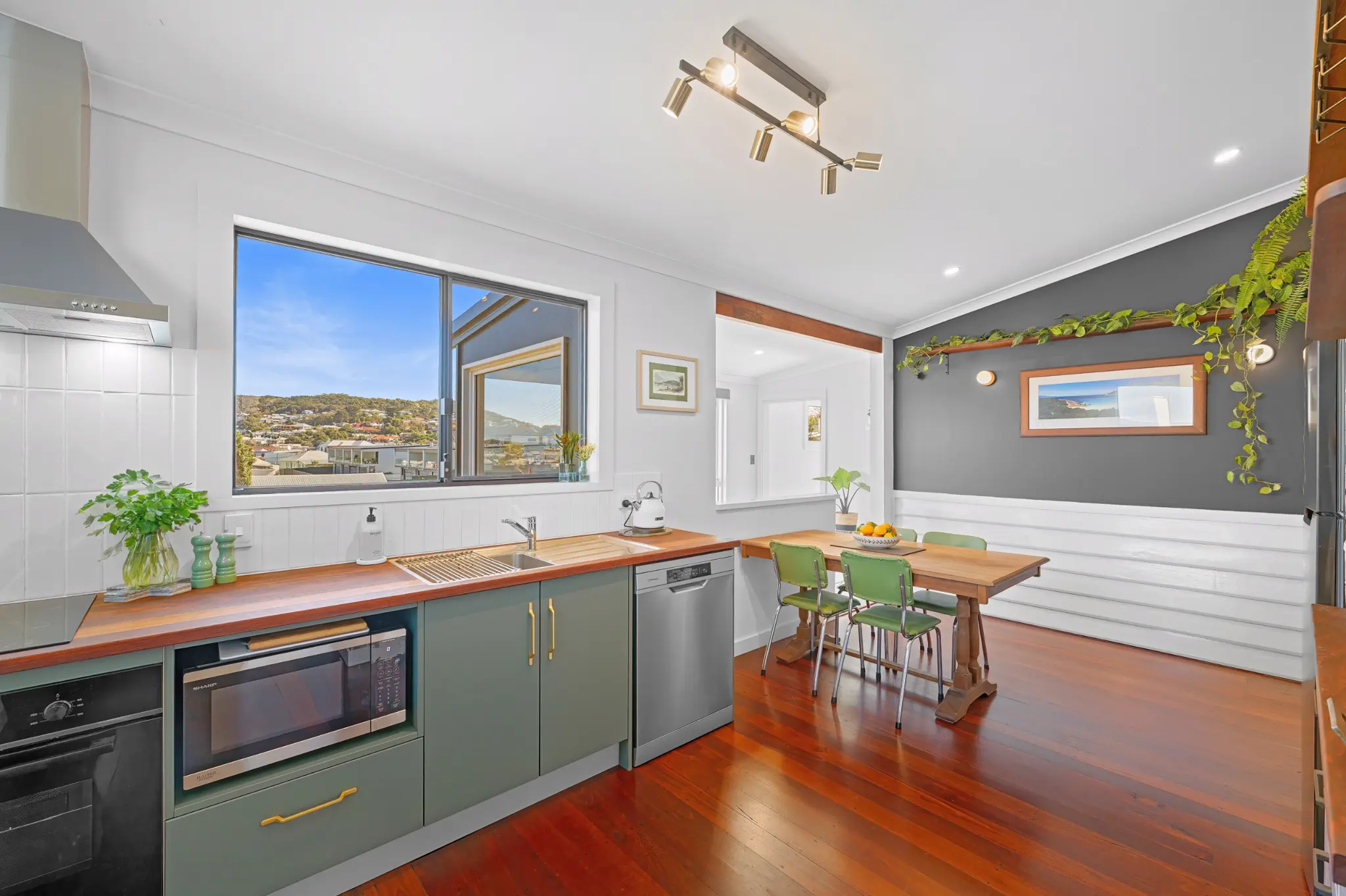 Green kitchen cabinetry with jarrah benchtop, dishwasher and harbour view through window