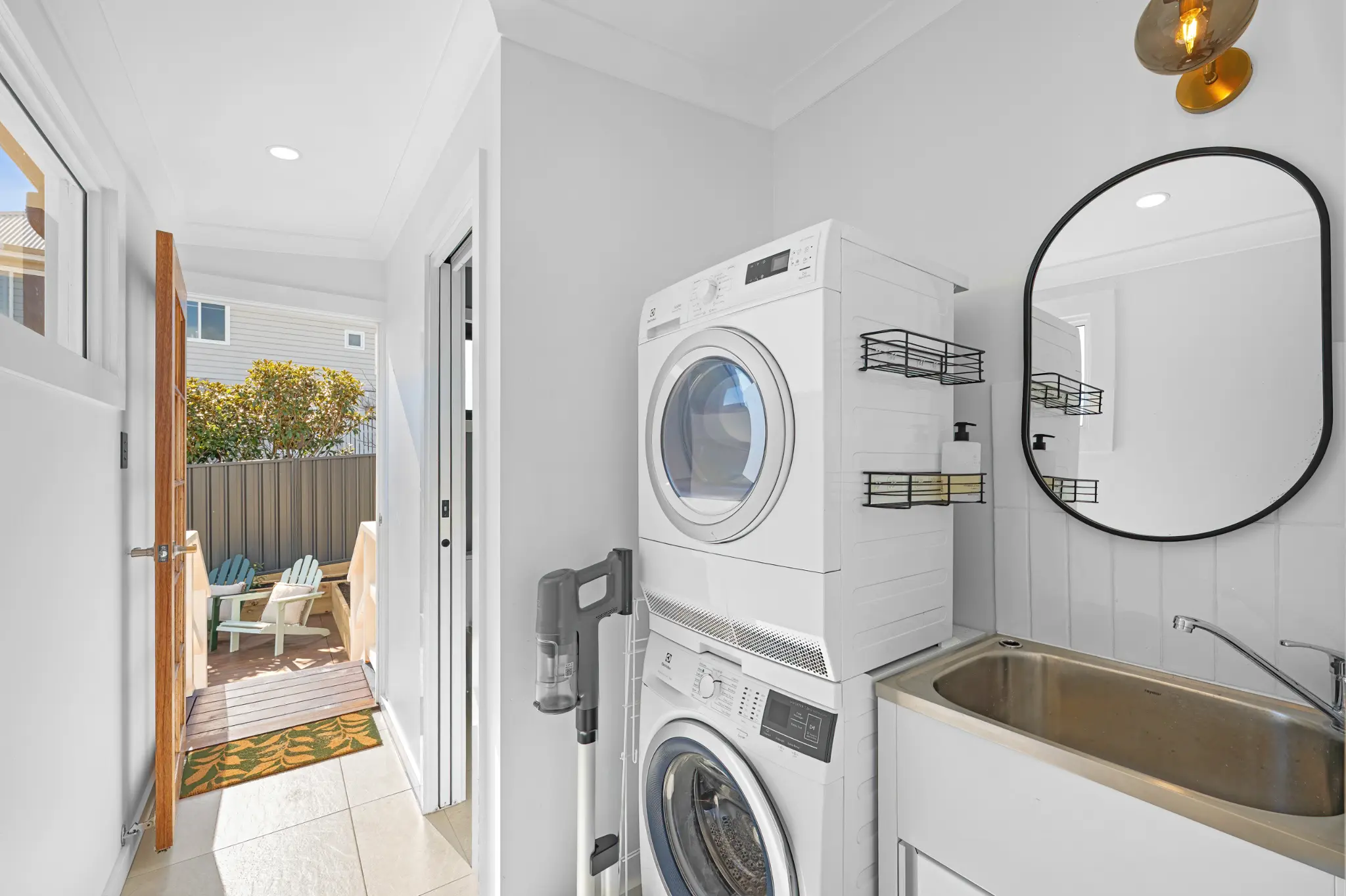 Laundry with stacked washer and dryer, laundry sink, wall shelves and door opening to timber deck and backyard