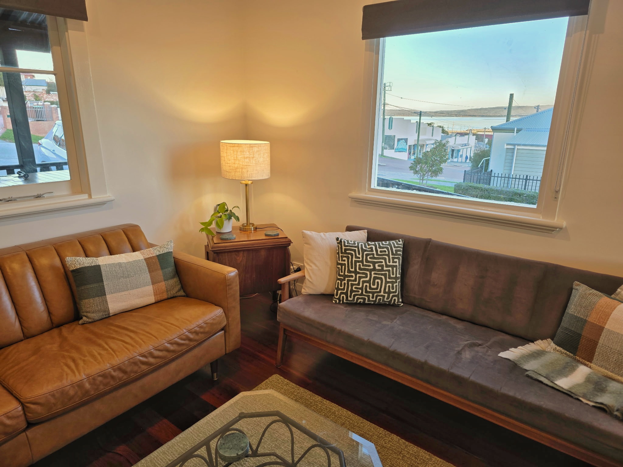 Intimate lounge with tan leather sofa and timber daybed, harbour glimpse through corner windows at dusk