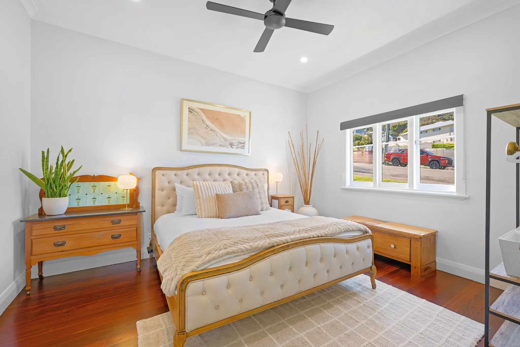 Master bedroom with tufted king bed, antique timber dresser, ceiling fan and polished jarrah floors